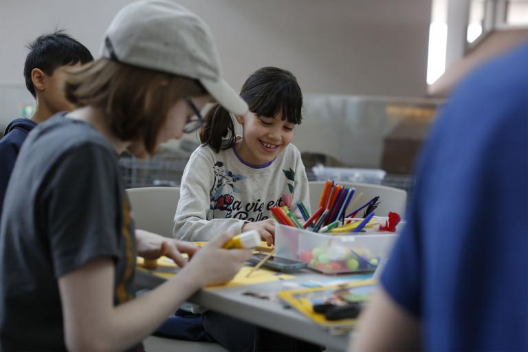 Des enfants d'âges différents sont assis autour d'une table en train de bricoler. Visibilité masquée.