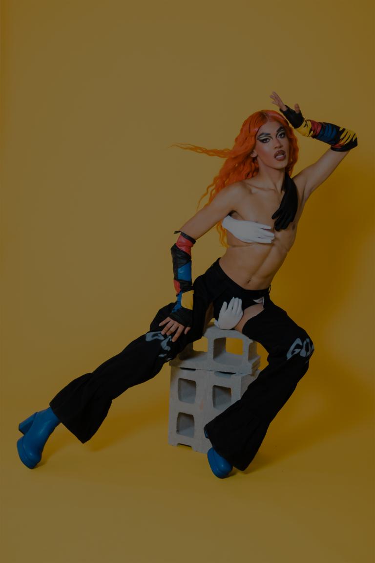 Homme avec une perruque orange, maquillage et un ensemble eccentrique. Visibilité masquée.