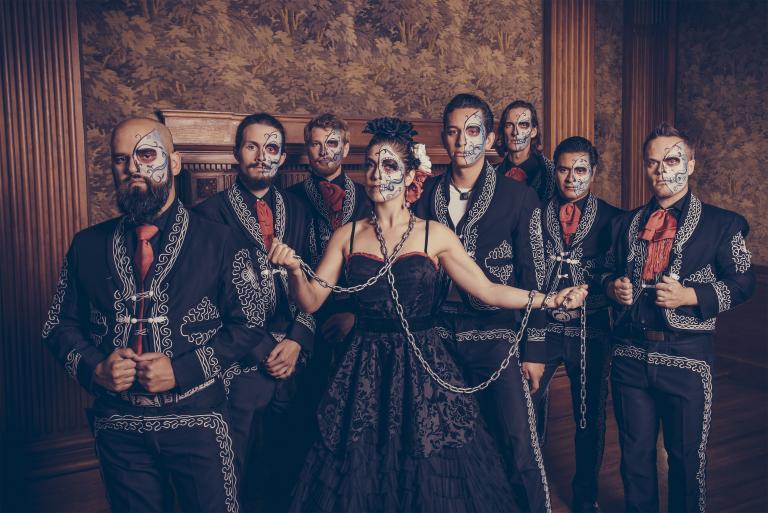 Les membres du The Mariachi Ghost, debout en rang, sont vêtus de costumes noirs assortis avec des détails cousus blancs et des cravates rouges. La moitié gauche de leur visage est peinte pour ressembler à un squelette. Visibilité masquée.