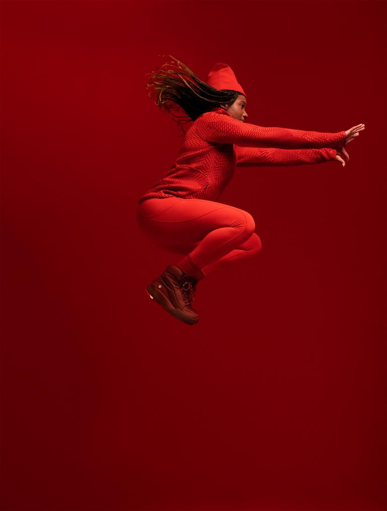 Une femme noire saute dans les airs, vêtue d'un uniforme olympique entièrement rouge. Visibilité masquée.