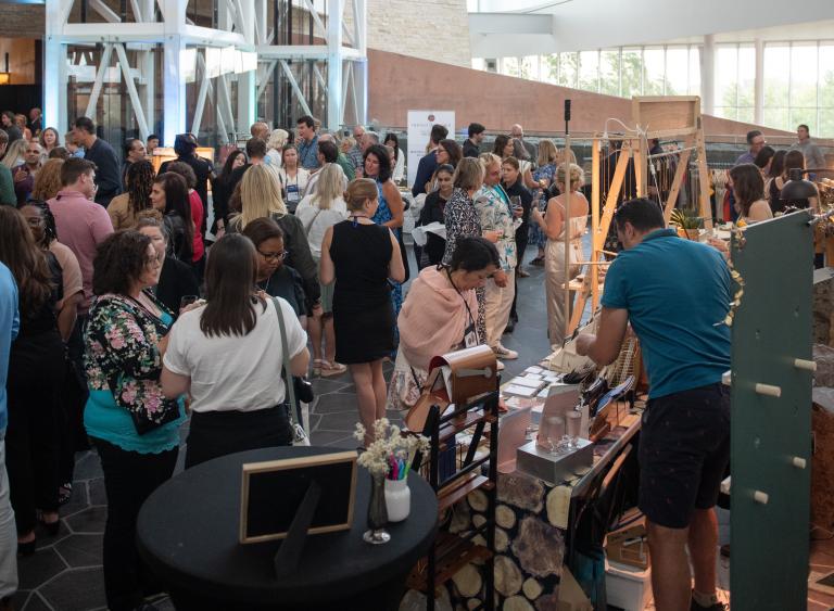 Un groupe de personnes se réunissant et discutant dans un grand hall. Une personne fait des achats à un kiosque. Visibilité masquée.