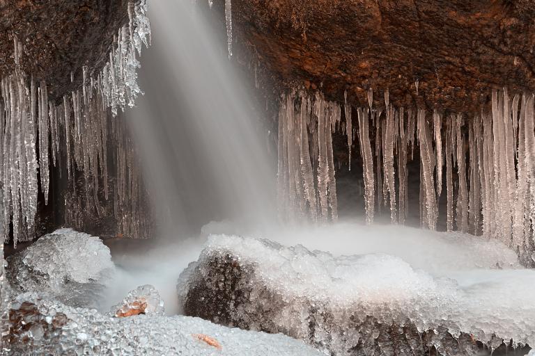 De l’eau est projetée sur des formations rocheuses à partir d’une ouverture invisible située au-dessus, ce qui crée un ensemble spectaculaire de stalactites et de monticules de glace sur les rochers. Visibilité masquée.