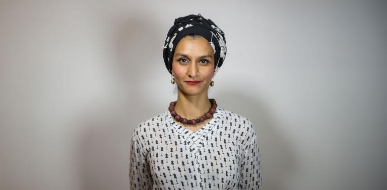 Une femme pakistanaise, Anna Abbas, portant un bandeau noir et blanc, un rouge à lèvres rouge, un collier brun épais et un chemisier noir et blanc regarde vers l'avant d'un air perplexe. Visibilité masquée.