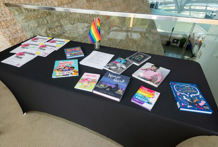 Une table avec une nappe noire et des livres colorés sur les 2SLGBTQI+. Visibilité masquée.