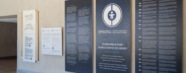 Grands panneaux bleu foncé avec texte et graphiques blancs exposés dans le Corridor communautaire du Musée canadien pour les droits de la personne. Le panneau central comporte un logo circulaire et commémore le 40e anniversaire du Centre canadien de protection de l'enfance. Les deux panneaux de chaque côté présentent du texte bilingue en anglais et en français.