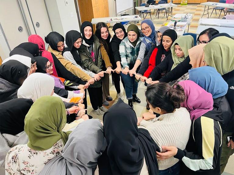Un groupe de femmes musulmanes souriantes formant un cercle et se tenant par la main. Visibilité masquée.