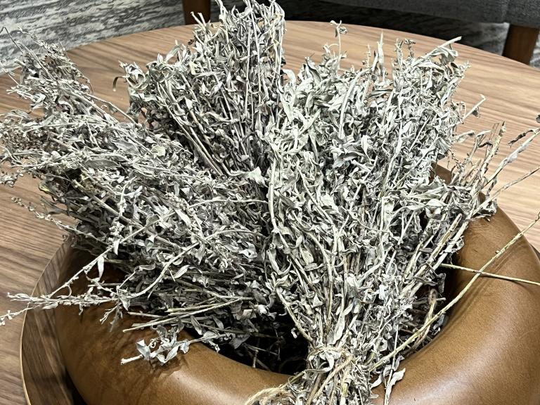 Un bouquet de sauge, dont les tiges sont attachées, est posé dans un petit bol en bois. Visibilité masquée.