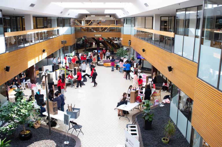 De nombreuses personnes sont rassemblées dans un espace intérieur ouvert où sont disposées des tables et des affiches. Visibilité masquée.