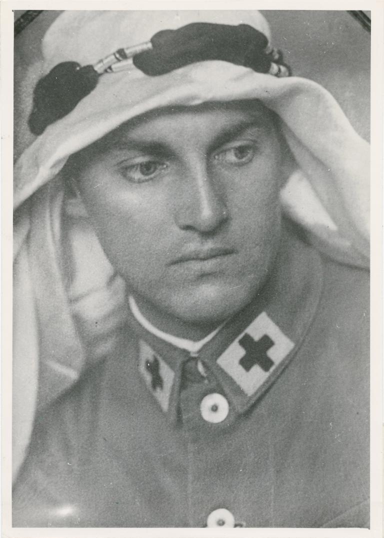 Un homme blanc en uniforme militaire avec une croix noire au bord du col porte un keffieh, une pièce en coton blanc portée au Moyen-Orient.