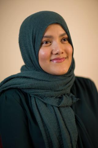 Un portrait photographique d’une femme aux yeux foncés dont les cheveux sont couverts d’un foulard vert foncé.